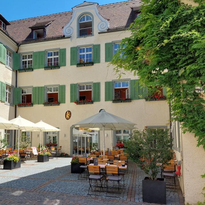Sie sehen die Sonnenterrasse mit Tischen, Stühlen und Sonnenschirmen im Innenhof im JUFA Hotel Meersburg am Bodensee in Baden-Württemberg in Deutschland.