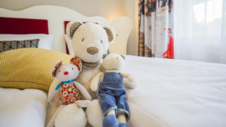 Sie sehen Stofftiere im Bett in einem FF4 Zimmer im JUFA Hotel Salzburg City. Der Ort für erholsamen Familienurlaub und einen unvergesslichen Winter- und Wanderurlaub.