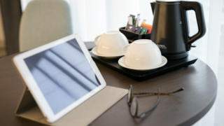 Sie sehen ein Tablet mit Teetassen und einem Wasserkocher am Tisch in einem Hotelzimmer. JUFA Hotels bietet kinderfreundlichen und erlebnisreichen Urlaub für die ganze Familie.