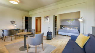 Sie sehen den Wohnbereich und Schlafbereich in einer Suite des JUFA Hotels Sigmundsberg. Der Ort für erholsamen Familienurlaub und einen unvergesslichen Winter- und Wanderurlaub.