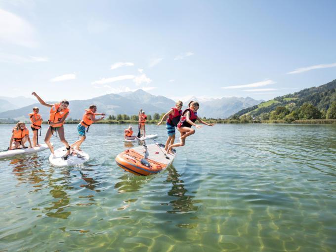Sie sehen Kinder im Zeller See, die von einem SUP ins Wasser springen. JUFA Hotels bietet erholsamen Familienurlaub und einen unvergesslichen Wanderurlaub.