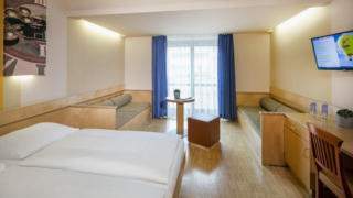 Sie sehen ein Familienzimmer mit Tisch und Doppelbett im JUFA Hotel Graz City***. Der Ort für erlebnisreichen Städtetrip für die ganze Familie und der ideale Platz für Ihr Seminar.