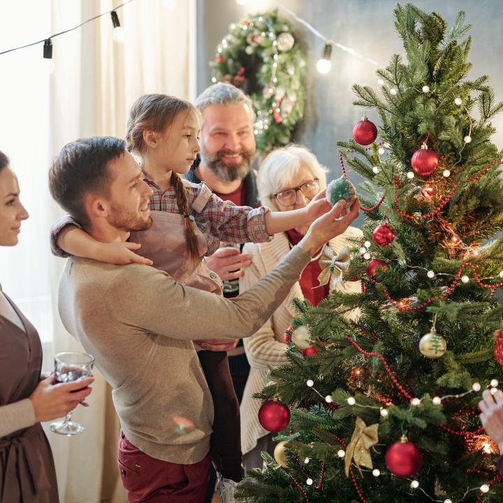 Sie sehen eine Familie mit Eltern, Kind und Großeltern neben einem bunt geschmückten Weihnachtsbaum in der Adventzeit.