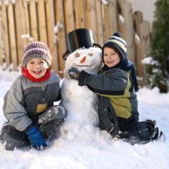 Sie sehen zwei Brüder beim Schneemann bauen im Winter mit JUFA Hotels.