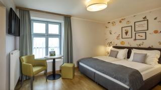 Sie sehen ein komfortables Boxspringbett als Doppelbett mit Sitzecke und Flachbild-TV im Appartement im JUFA Hotel Schilcherland*** in der Steiermark.