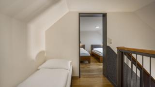 Sie sehen drei Einzelbetten im oberen Stock eines Galeriezimmers für 5 Personen im JUFA Hotel Schilcherland*** in der Steiermark.