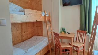 Sie sehen einen kleinen Tisch mit zwei Stühlen mit einem Fernseher darüber und ein Etagenbett aus Holz im LowBudget 4 Zimmer im JUFA Hotel Bad Aussee***.
